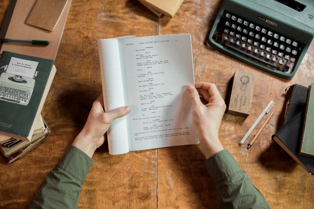 Hands holding an open screenplay at a writer's desk