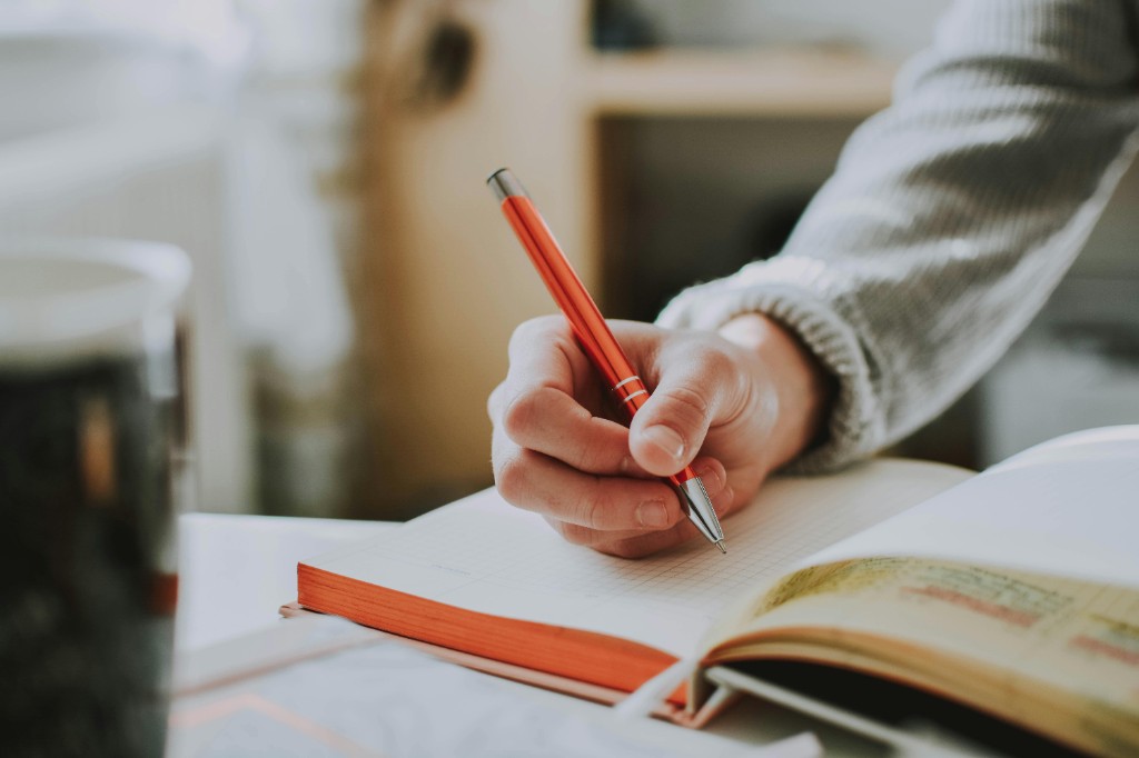 Hand writing notes with a red pen in a notebook